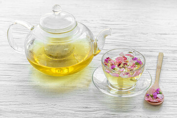 Teapot and cup with floral tea on light background