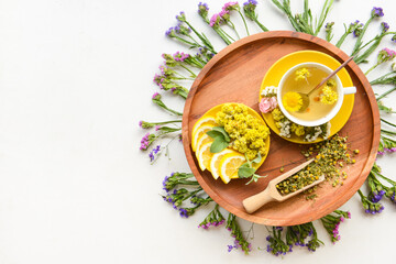 Cup with floral tea, flowers and lemon on light background