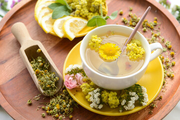 Cup with floral tea, flowers and lemon on light background