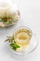 Teapot and cup with floral tea on light background