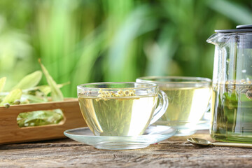 Teapot and cups with herbal tea on table against blurred background