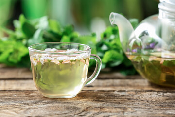 Teapot and cup with floral tea on table against blurred background