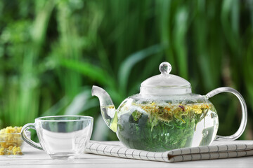 Teapot and cup with floral tea on table against blurred background