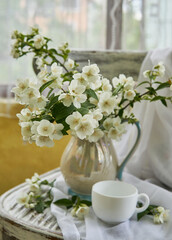 Fototapeta na wymiar Jasmine flowers in a white vase. Stillife with jasmine and cup of coffee.