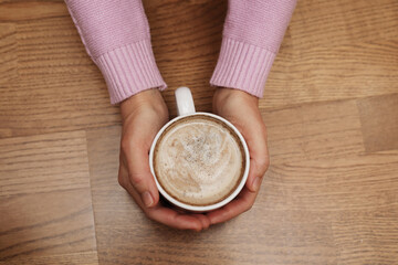 A cup of delicious coffee in female hands. A warm drink for the holiday. Cozy coffee break. For wallpaper and background.