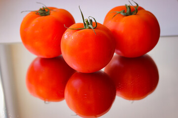 Several red tomatoes on a mirror surface