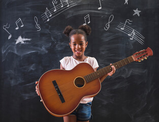 Beautiful mixed race schoolgirl playing the guitar while in music class in school