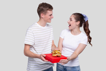 Couple Holding Present Looking at Each Other. Couple Forwording Gift to Camera. Couple with Gift in Hands.