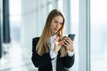 Smiling businesswoman using phone in office. Business entrepreneur looking at her mobile phone and smiling.