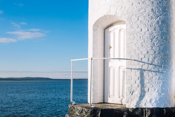 Obraz premium The white door of the lighthouse against the background of the sea coast.