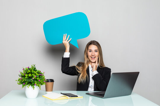 Portrait of a young business woman sitting at the office desk with empty speech bubbles above her head