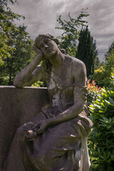 eine Frau in tiefer Trauer lehnt an einem Grabstein