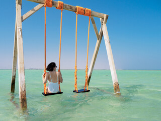 Young woman sat on a swing in the ocean - white sand and turquoise water of the Giftun islands, Egypt