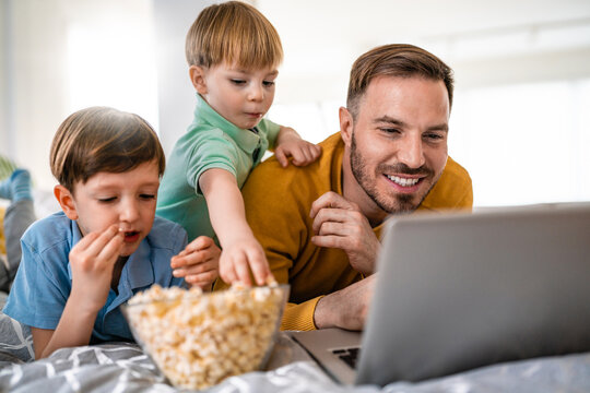 Overjoyed little children resting on bed with smiling dad, enjoying funny movie on computer together