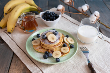 fresh pancakes with berries and bananas on a plate, morning breakfast with tea and milk
