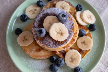 fresh pancakes with berries and chopped bananas on a plate, sprinkled with powdered sugar, morning breakfast