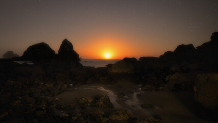 The Moon Setting Over a Rocky Beach at Night - 402435366