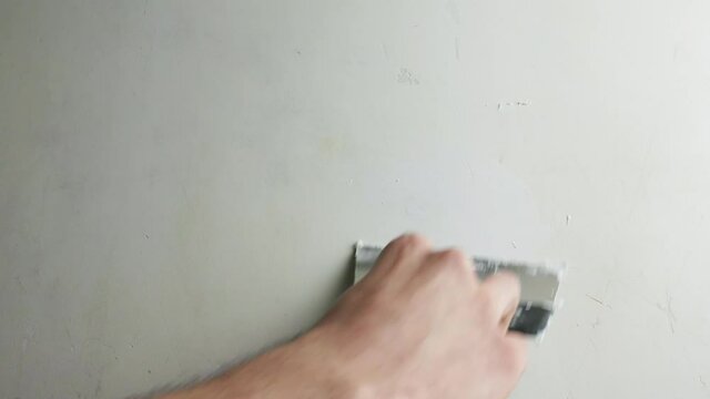 Hand with a spatula smooths out the unevenness of the concrete wall. Wall putty and repair.