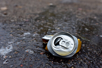 Crumpled a beer can on asphalt with spilled alcohol. Discarded broken carbonated drink can at a...