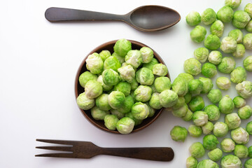 Brussels sprouts lies on the table and in a wooden bowl, next to a wooden fork and spoon