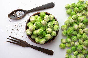 Brussels sprouts lies on the table and in a wooden bowl, next to them lie a wooden fork, a spoon and salt in a spoon