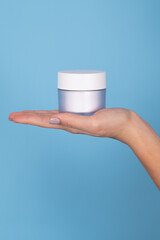 Cropped shot of woman holding jar of moisturizing cream isolated on blue. Background with empty space for your design