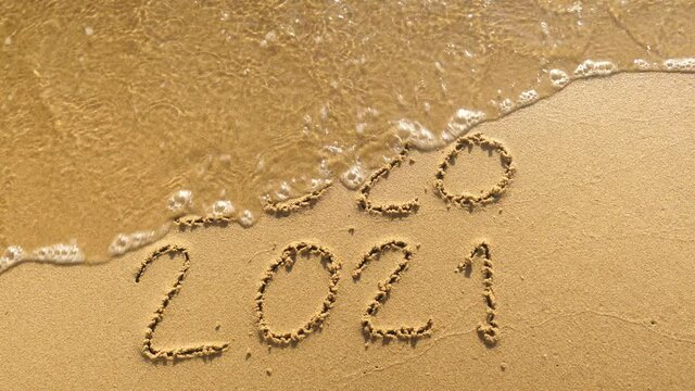 Message Year 2020 replaced by 2021 written on beach sand background. Good bye 2020 hello to 2021 Lapping waves happy New Year coming concept
