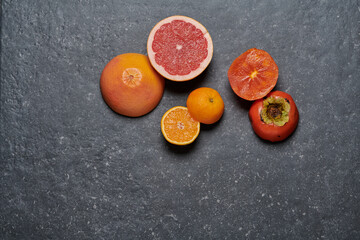 Top view of a group of orange, grapefruit and kaki on dark grey stone background