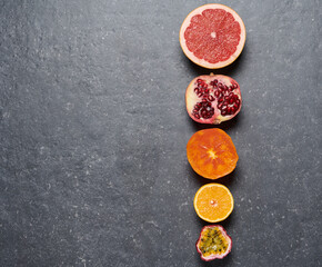Line of orange, grapefruit, pomegrade, passion fruit and kaki on grey background