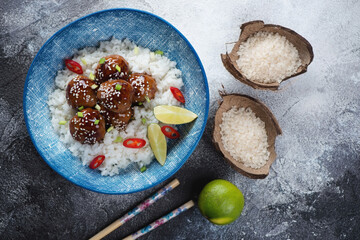 Blue plate with asian style rice and meatballs in teriyaki sauce, top view on a grey stone background, horizontal shot