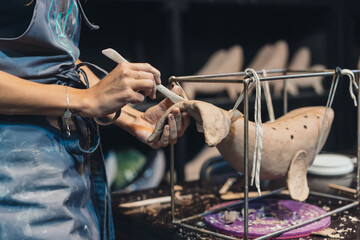 Close-up view of female hands gently handling a clay whale in workshop.