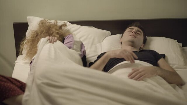 Caucasian woman waking up of man's snore in bedroom. Adult couple family sleeping at home in bed. Snoring and relaxation. Health care problems.