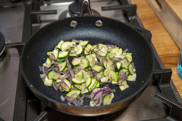 A frying pan in a kitchen frying onions and cucumber slices