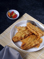 Banana fritters or fried banana or pisang goreng served in white plate with chilies. Typical Indonesian snack. Also easy to find as street food in Indonesia. Sweet, tasty and bit crunchy.