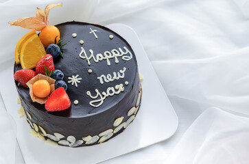 Chocolate cake topped with orange, strawberry, blueberry and Cape Gooseberry on white cloth background,