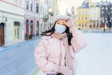 Positive emotion active lifestyle. Asian woman wearing mask for protect pm2.5 and Covid-19 virus outdoor at european city on the ice rink trying ride on ice skates in sunny frozy day.