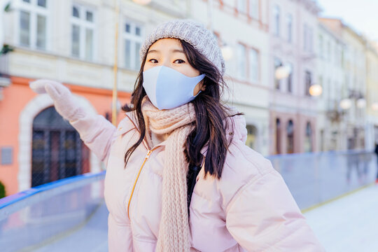 Positive emotion active lifestyle. Asian woman wearing mask for protect pm2.5 and Covid-19 virus outdoor at european city on the ice rink trying ride on ice skates in sunny frozy day. - Powered by Adobe