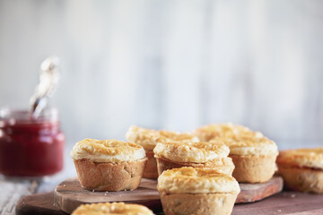 Fresh meat pies on a rustic wood cutting board with ketchup in the background. Selective focus on center pie with extreme blurred foreground and background. Free space for text available