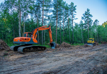 Excavator clearing forest for new development. Orange Backhoe modified for forestry work. Tracked heavy power machinery for forest and peat industry. Logging, road construction in forests