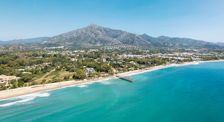 Unique aerial view of luxury and exclusive area in Marbella, golden mile beach, view of Puente Romano Bridge and in background famous La Concha mountain. Emerald water colour  - obrazy, fototapety, plakaty