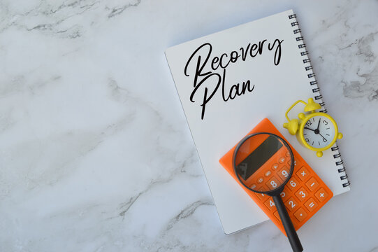 Top view of calculator, magnifying glass, clock and calculator written with text RECOVERY PLAN. Business and financial concept. 