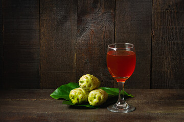 Noni juice and noni fruit with leaf on wooden background. Healthy concept.