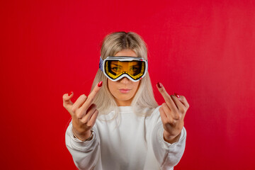 Portrait girl skier wearing glasses doing middle finger gesture. Close-up snowboarder on red background showing middle finger doing fuck you bad expression