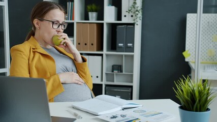 Slow motion of young pregnant businesswoman eating apple and using laptop then relaxing in office during work break. Nutrition and pregnancy concept. - Powered by Adobe
