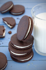 Homemade chocolate stuffed cookies stacked next to glass with fresh milk on blue rustic wooden table