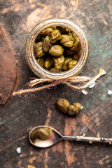 Capers Marinated capers in a jar on wooden background. vertical image, place for text. Delicious ingredients for cooking Mediterranean, Italian, Spanish, French cuisine. Pickled capers. Canned capers