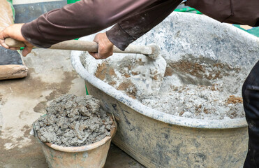 Man hands working and holding hoe mix cement and sand in a gray plastic bowl