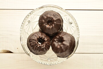 Three sweet chocolate marshmallows on a crystal plate, close-up, on a wooden table.