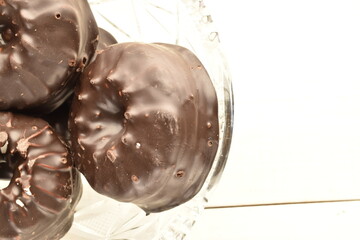 Three sweet chocolate marshmallows on a crystal plate, close-up, on a wooden table.