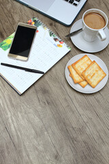 Biscuits on plate, a cup of latte, 2021 desk calendar part, smartphone, pen, and part of blurry laptop on the table. Flat lay, top view